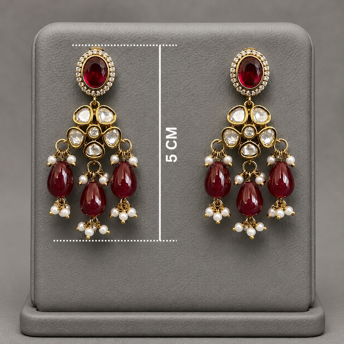 A pair of gold-plated dangle earrings with red gemstones and clear stones, displayed on a gray stand with a 5 cm height measurement overlay.