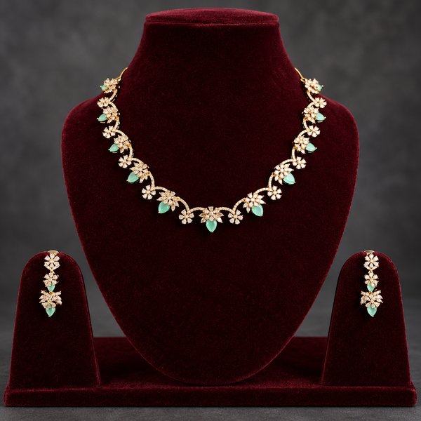 Gold floral jewelry set with mint green stones, displayed on a dark red velvet necklace bust and matching stand, with matching drop earrings on side stands against a dark gray background.