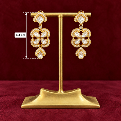 Gold-plated statement dangle earrings with clear crystals, displayed on a gold stand against a dark red background, with a size marker indicating 4.4 cm height.