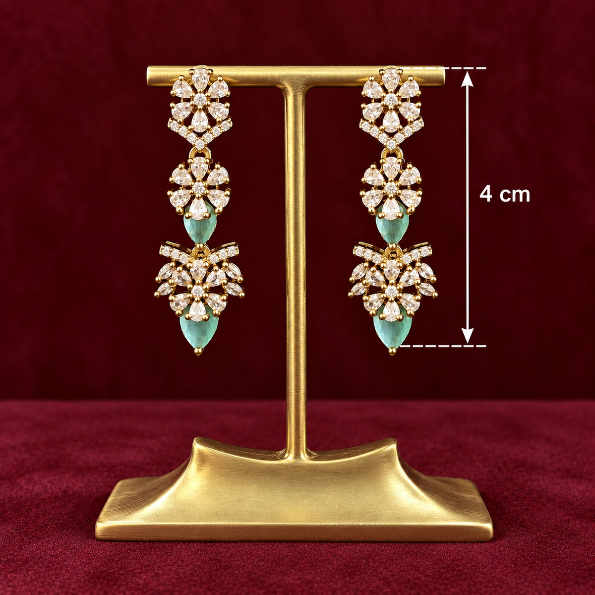 Gold-tone dangle earrings with clear floral stones and light blue teardrop accents, displayed on a gold stand against a dark red background, with a 4 cm height measurement overlay.