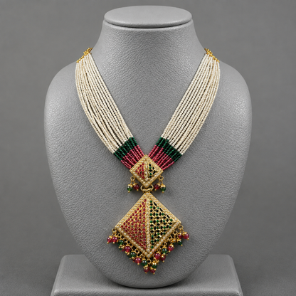 A traditional Indian statement necklace displayed on a gray mannequin bust. The necklace features a multi-strand cream bead collar, green and magenta beaded accents at the collar, and a large central diamond-shaped pendant decorated with gold, red, and green stones.