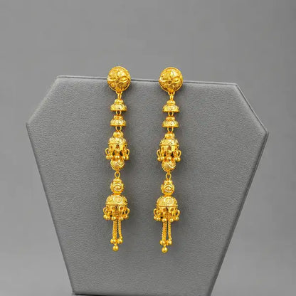 A pair of ornate gold dangle earrings displayed on a gray jewelry stand against a neutral gray background.