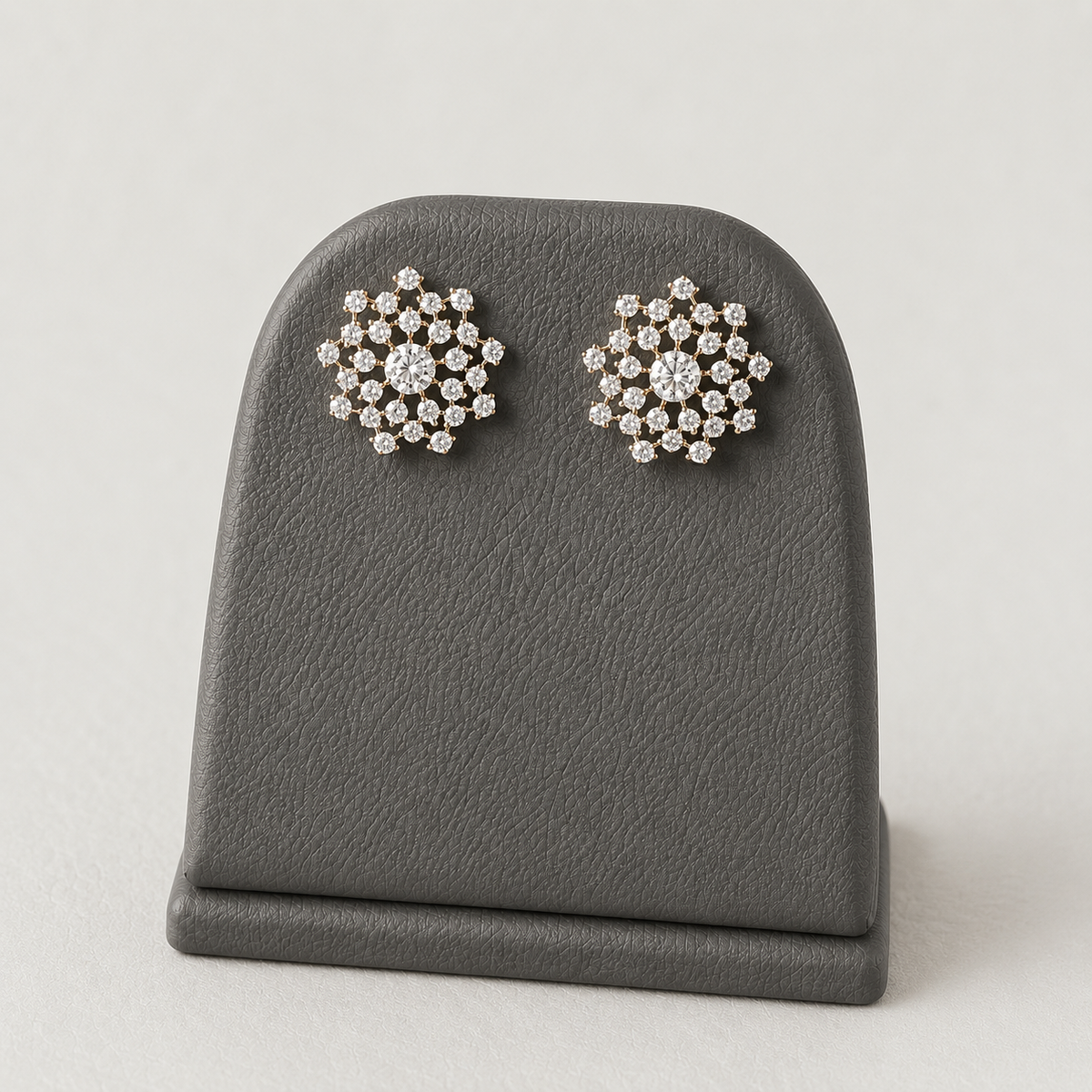Pair of gold-tone American Diamond floral stud earrings displayed on a stand against a rich maroon background.