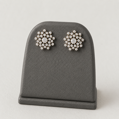 Pair of gold-tone American Diamond floral stud earrings displayed on a stand against a rich maroon background.