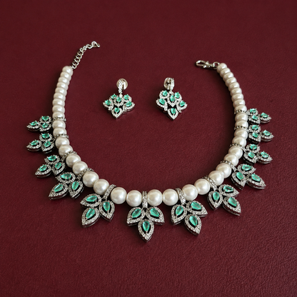 A pearl and silver-tone jewelry set featuring a statement necklace and matching earrings, decorated with green teardrop-shaped stones, displayed on a dark red textured background.