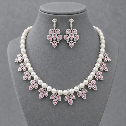A pearl and silver jewelry set featuring a statement necklace and matching drop earrings, decorated with pink gemstone accents, displayed on a gray jewelry bust.