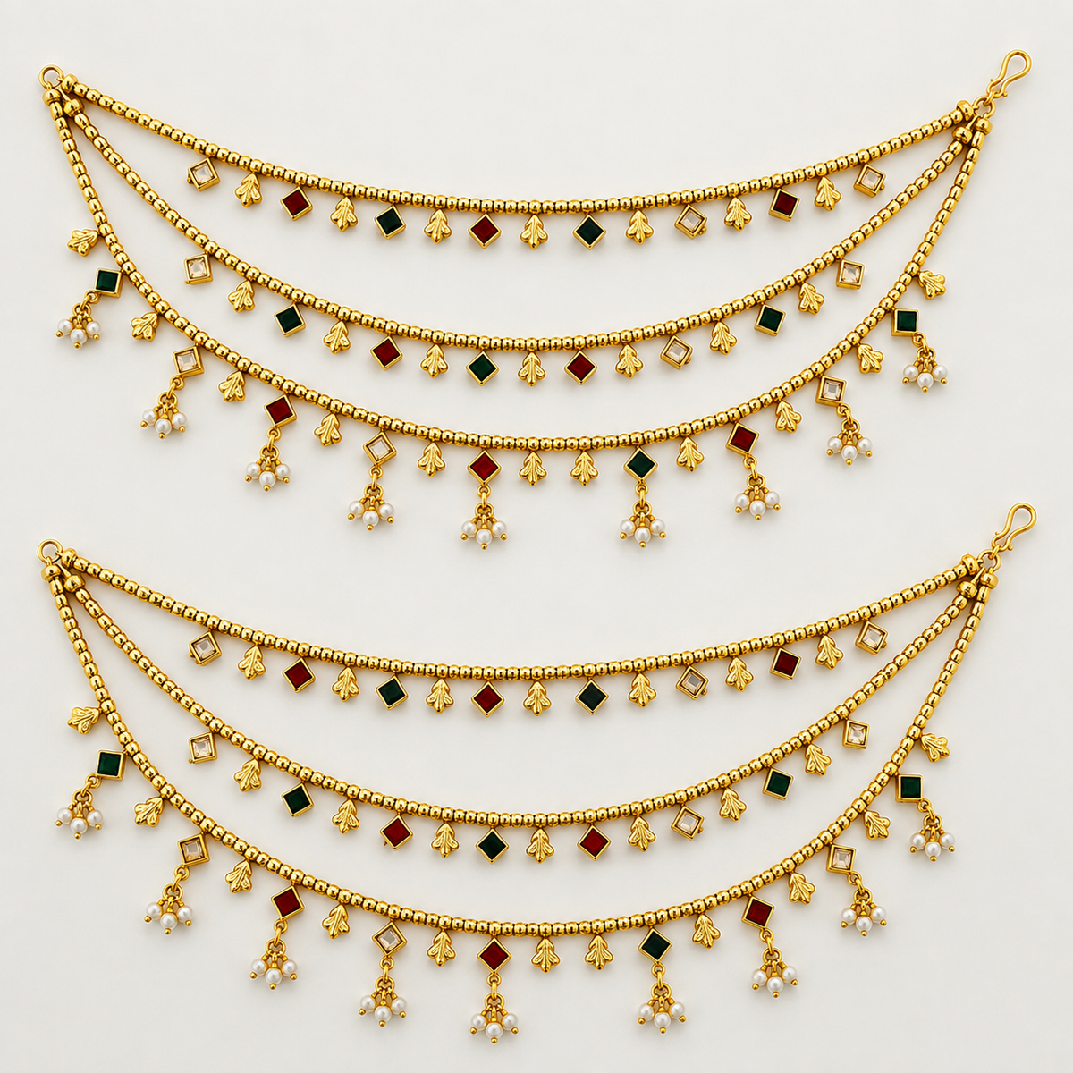 Two gold-toned traditional Indian jewelry pieces, likely bangles or decorative necklaces, featuring triple curved rows of beads, small floral motifs, and dangling charms with red, green, and white stones on a plain light background.